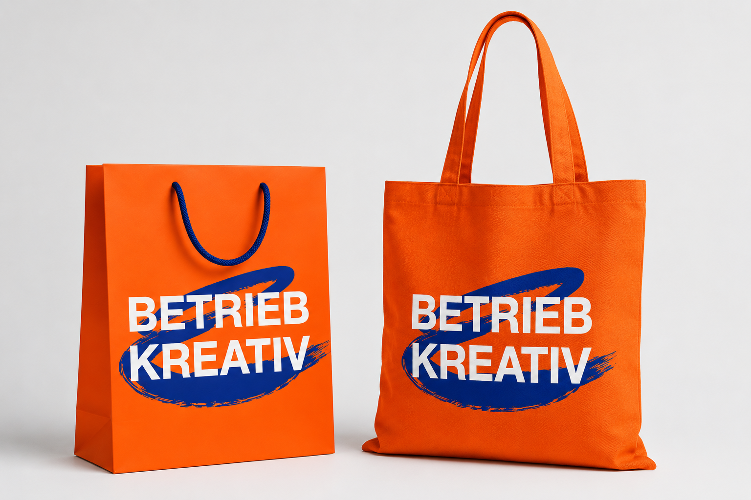 Bedruckte Tragetaschen aus Papier und Stoff in Orange mit blauem Pinselstrich-Logo — Papiertüte und Baumwoll-Stofftasche als Werbeartikel von Betrieb Kreativ